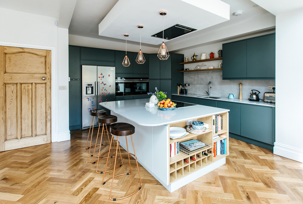 Medium sized contemporary l-shaped open plan kitchen in Other with a double-bowl sink, flat-panel cabinets, grey splashback, stainless steel appliances, light hardwood flooring, an island, beige floors and white worktops.