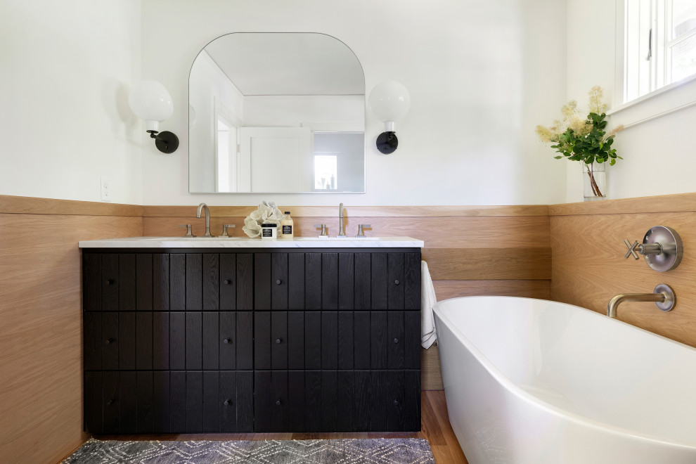 Design ideas for a rural bathroom in Minneapolis with black cabinets, a freestanding bath, white walls, light hardwood flooring, a submerged sink, marble worktops, brown floors, white worktops, double sinks and a built in vanity unit.