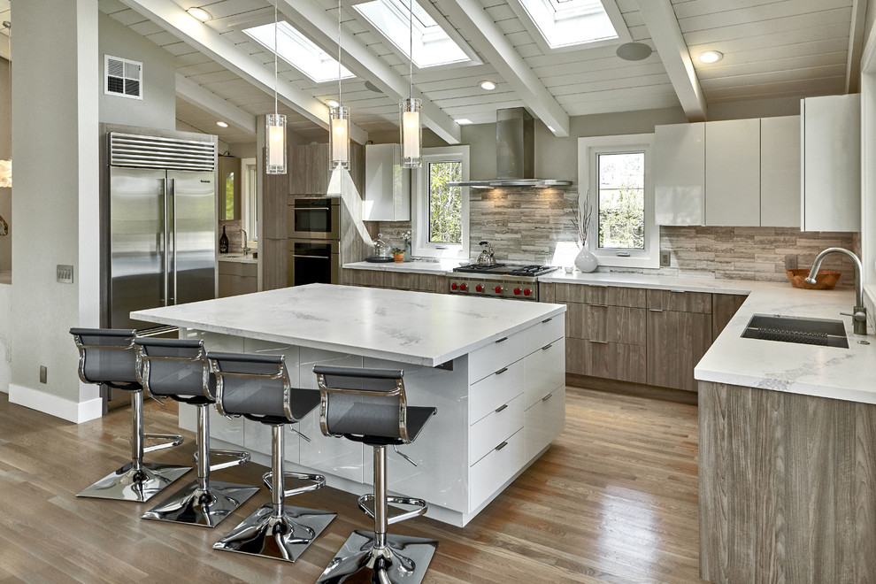 Large trendy l-shaped medium tone wood floor and brown floor open concept kitchen photo in San Francisco with an undermount sink, flat-panel cabinets, medium tone wood cabinets, quartzite countertops, gray backsplash, travertine backsplash, stainless steel appliances, an island and white countertops
