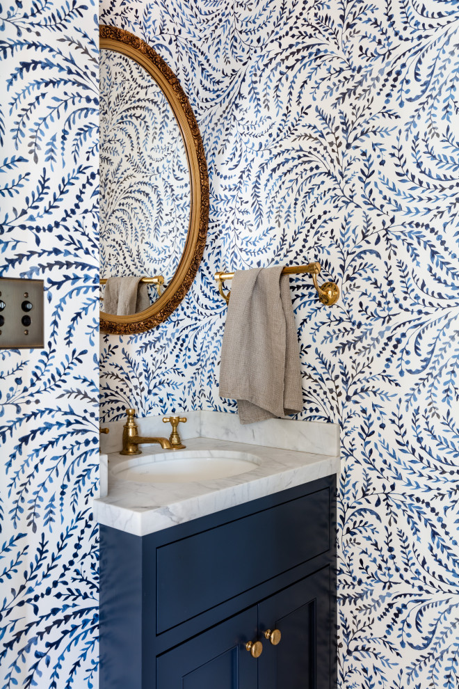 Small traditional cloakroom in Seattle with beaded cabinets, blue cabinets, a one-piece toilet, blue walls, light hardwood flooring, a submerged sink, marble worktops, brown floors, white worktops, a built in vanity unit and wallpapered walls.