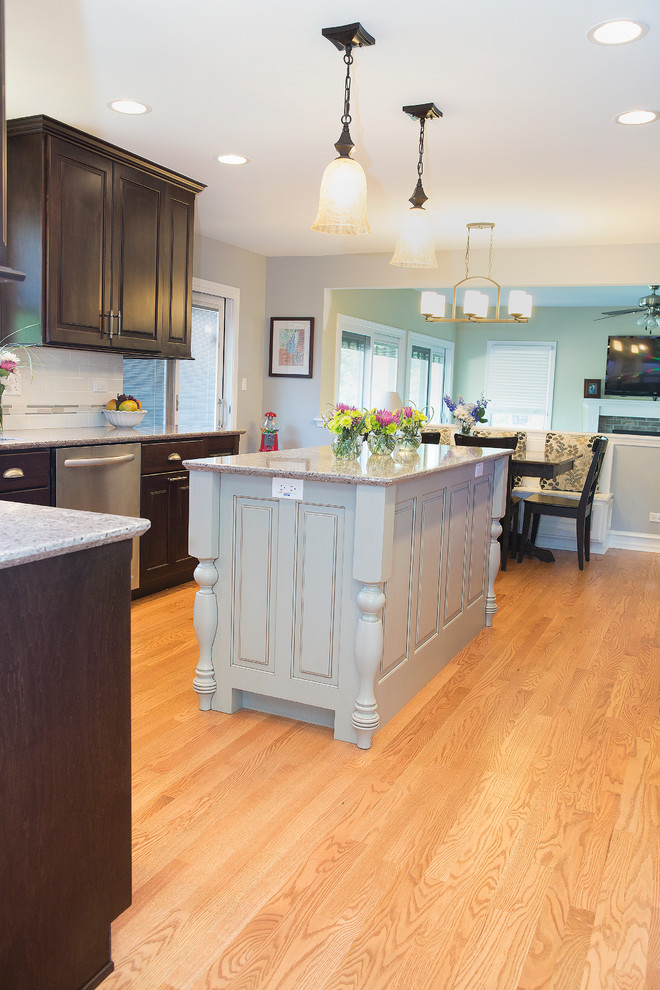 Example of a mid-sized transitional u-shaped light wood floor enclosed kitchen design in Chicago with an undermount sink, raised-panel cabinets, dark wood cabinets, quartz countertops, beige backsplash, ceramic backsplash, stainless steel appliances and an island