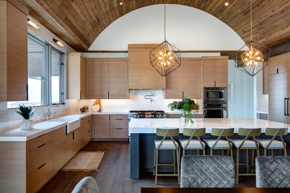 Large contemporary u-shaped open plan kitchen in Salt Lake City with a farmhouse sink, flat-panel cabinets, marble benchtops, marble splashback, stainless steel appliances, dark hardwood floors, with island, brown floor, medium wood cabinets, white splashback and white benchtop.
