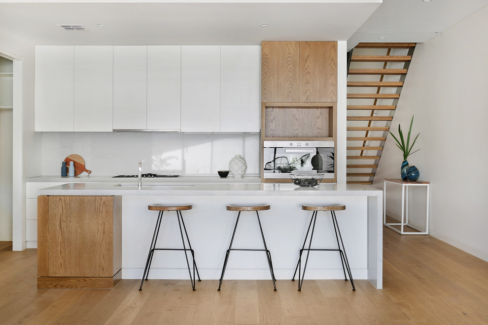 Design ideas for a large contemporary galley kitchen in Melbourne with an undermount sink, white cabinets, quartz benchtops, grey splashback, stone slab splashback, stainless steel appliances, light hardwood floors, with island, beige floor, flat-panel cabinets and grey benchtop.