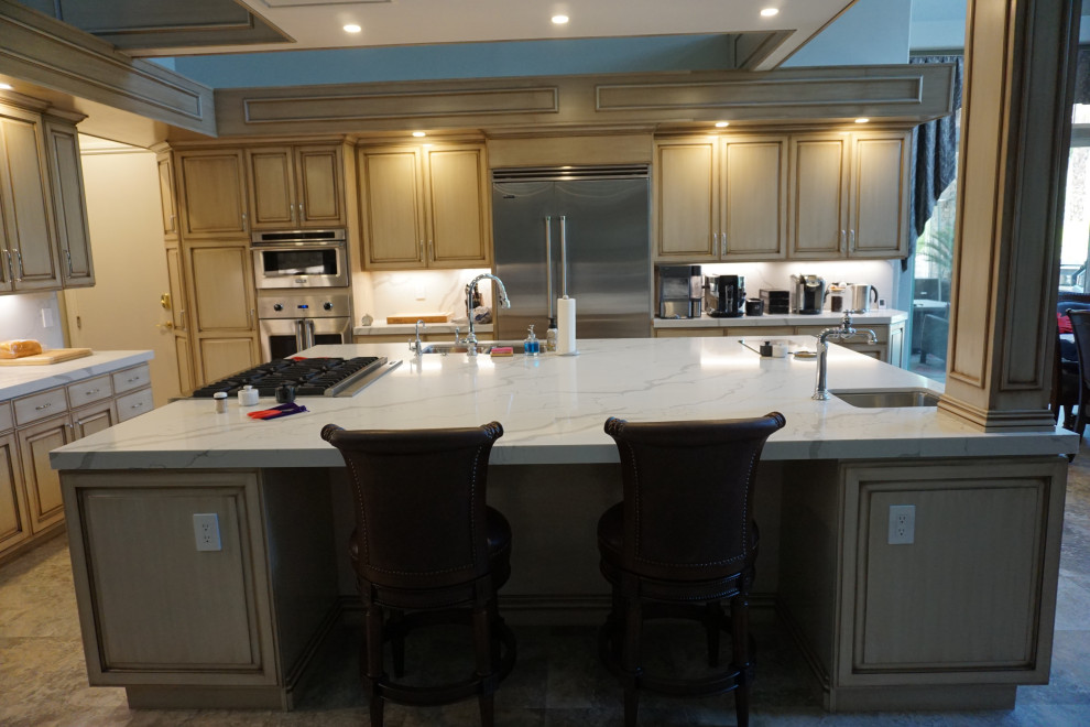 This is an example of an expansive modern l-shaped open plan kitchen in Las Vegas with an undermount sink, raised-panel cabinets, beige cabinets, quartzite benchtops, white splashback, stainless steel appliances, travertine floors, with island, multi-coloured floor and white benchtop.