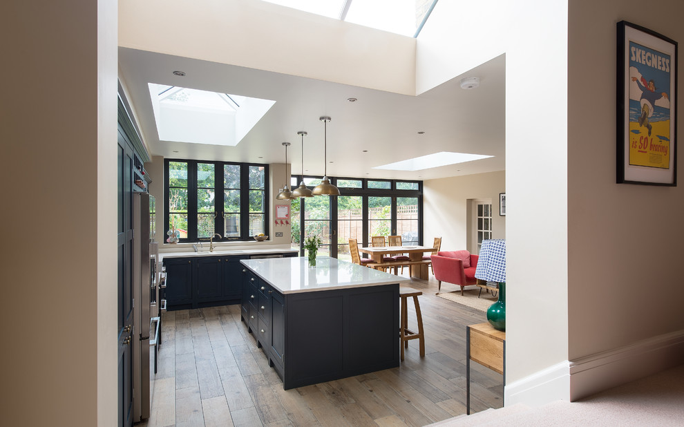 This is an example of a mid-sized traditional open plan kitchen in Gloucestershire with shaker cabinets, blue cabinets, light hardwood floors and with island.