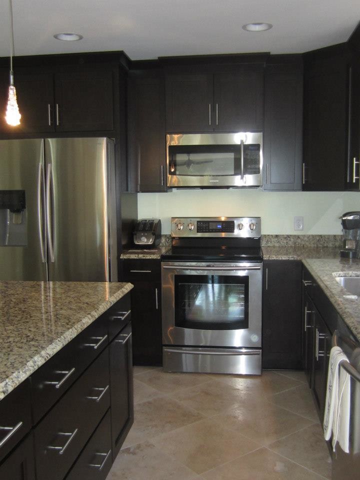 Mid-sized l-shaped ceramic tile eat-in kitchen photo with a double-bowl sink, dark wood cabinets, granite countertops, stainless steel appliances and an island