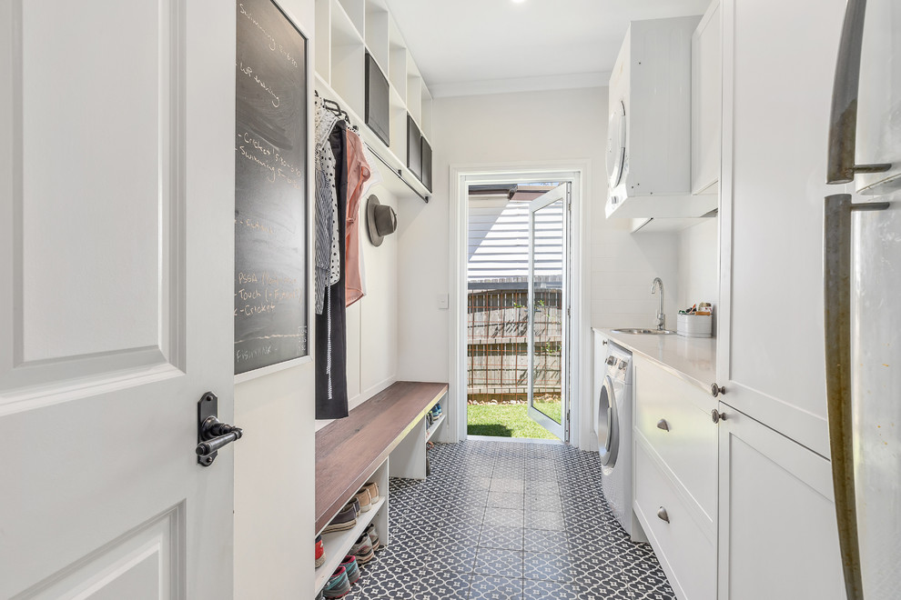 Mid-sized transitional single-wall utility room in Sydney with shaker cabinets, white cabinets, quartz benchtops, white walls, ceramic floors, a stacked washer and dryer, multi-coloured floor, white benchtop and a drop-in sink.