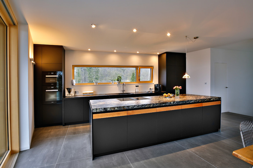 Inspiration for a large modern galley eat-in kitchen in Stuttgart with an undermount sink, flat-panel cabinets, black cabinets, granite benchtops, white splashback, window splashback, black appliances, cement tiles, with island, black floor and black benchtop.