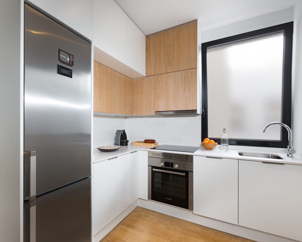 Inspiration for a small scandinavian l-shaped kitchen in Madrid with a single-bowl sink, flat-panel cabinets, white cabinets, white splashback, stainless steel appliances, light hardwood floors, no island and white benchtop.