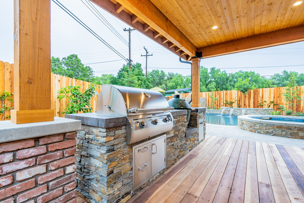 This is an example of a mid-sized country backyard patio in Orange County with an outdoor kitchen, natural stone pavers and a roof extension.
