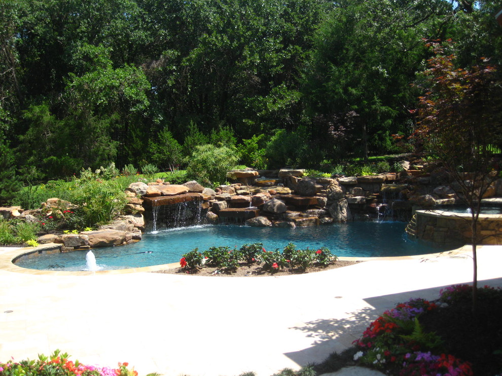 Large traditional backyard kidney-shaped lap pool in Dallas with a water feature and concrete pavers.
