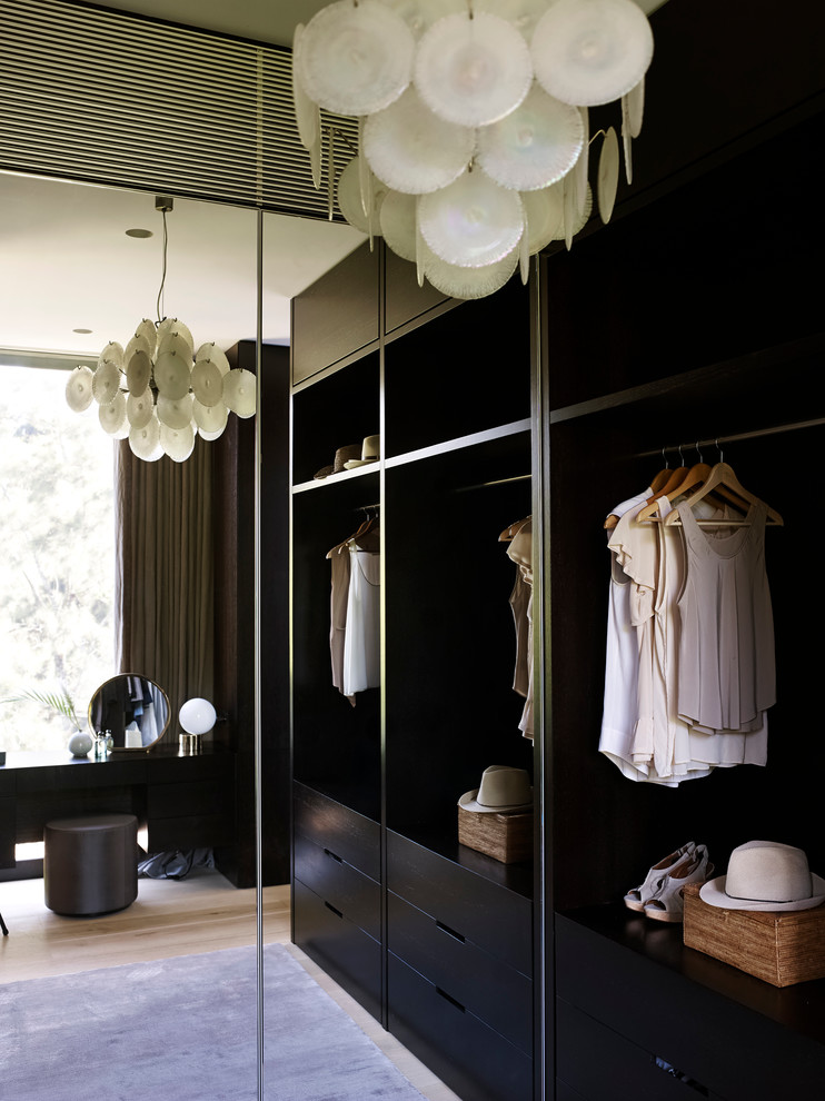 This is an example of a small contemporary gender-neutral walk-in wardrobe in Sydney with flat-panel cabinets and dark wood cabinets.