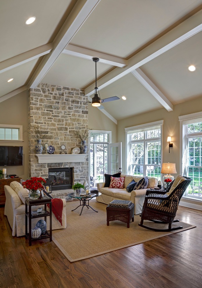 Photo of a mid-sized traditional open concept family room in St Louis with beige walls, light hardwood floors, a two-sided fireplace, a stone fireplace surround and a wall-mounted tv.