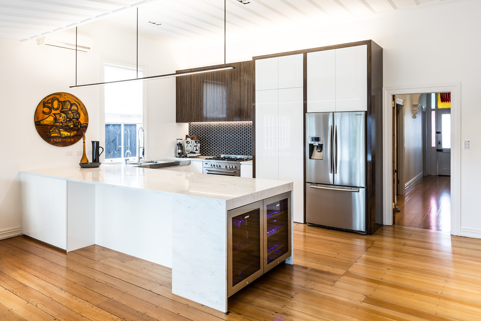 Photo of a contemporary u-shaped eat-in kitchen in Auckland with an undermount sink, flat-panel cabinets, white cabinets, solid surface benchtops, black splashback, mosaic tile splashback and stainless steel appliances.