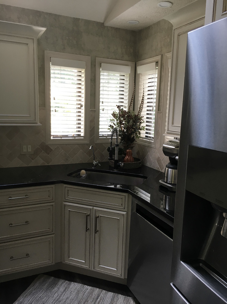 Large transitional u-shaped laminate floor and gray floor eat-in kitchen photo with an undermount sink, recessed-panel cabinets, white cabinets, granite countertops, white backsplash, ceramic backsplash, stainless steel appliances, an island and black countertops