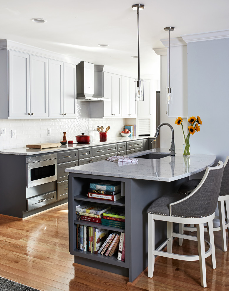 Photo of a mid-sized transitional l-shaped eat-in kitchen in Chicago with an undermount sink, recessed-panel cabinets, white cabinets, quartz benchtops, white splashback, ceramic splashback, stainless steel appliances, medium hardwood floors, a peninsula, brown floor and grey benchtop.