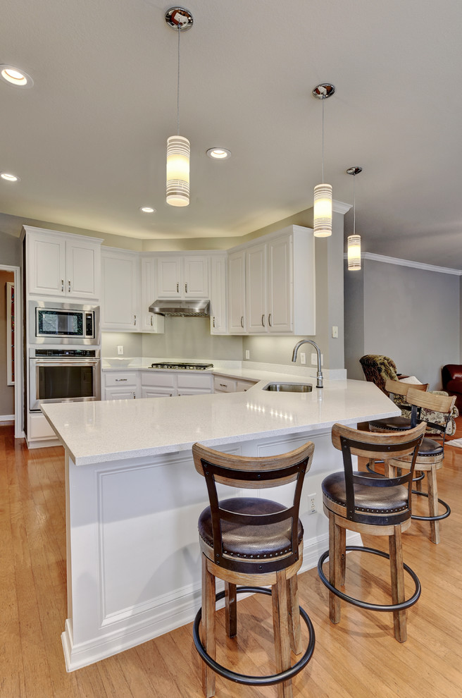 Inspiration for a mid-sized transitional u-shaped light wood floor eat-in kitchen remodel in Austin with an undermount sink, white cabinets, quartz countertops, white backsplash, stone slab backsplash, stainless steel appliances, a peninsula and raised-panel cabinets