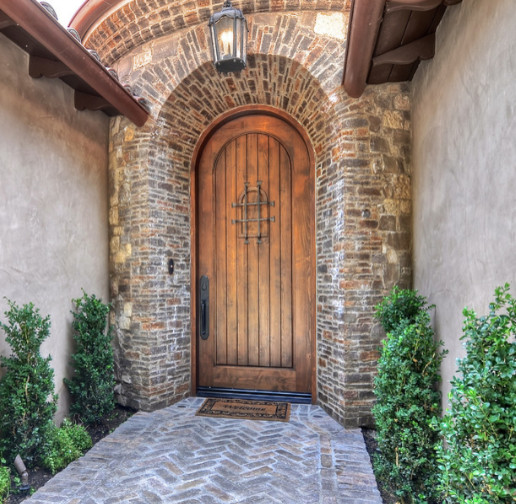 Inspiration for a large mediterranean front door in Los Angeles with brown walls, a single front door, a dark wood front door, brick floors and brown floor.