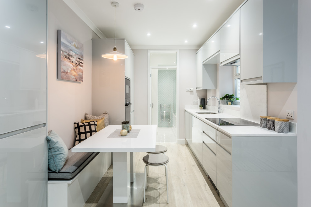Photo of a small contemporary galley open plan kitchen in London with a drop-in sink, flat-panel cabinets, grey cabinets, solid surface benchtops, panelled appliances, laminate floors, beige floor and white benchtop.
