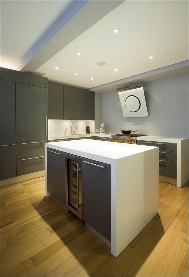 Design ideas for a mid-sized modern l-shaped eat-in kitchen in New York with an undermount sink, flat-panel cabinets, grey cabinets, solid surface benchtops, white splashback, stainless steel appliances, light hardwood floors, with island and brown floor.