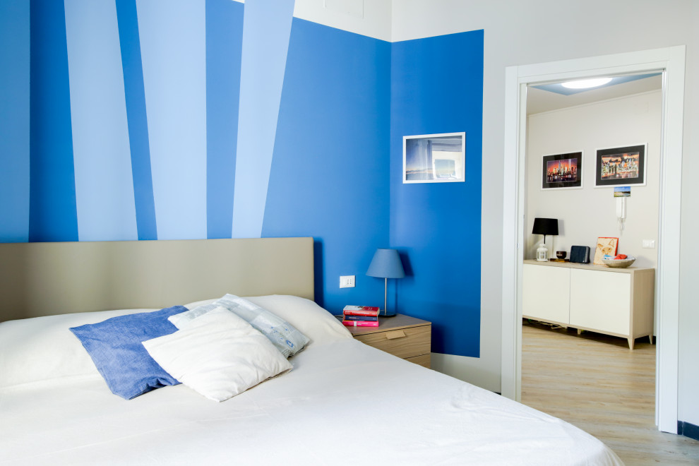 Cette photo montre une chambre parentale tendance avec un mur bleu, sol en stratifié, un sol beige et différents habillages de murs.