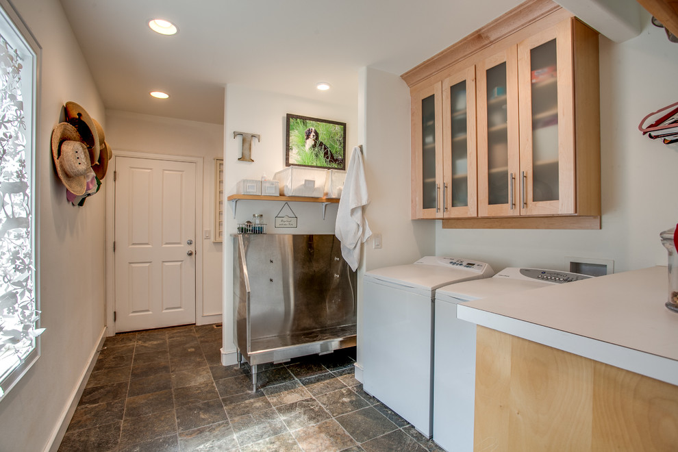 This is an example of a country single-wall laundry room in Seattle with an utility sink, glass-front cabinets, light wood cabinets, white walls and a side-by-side washer and dryer.