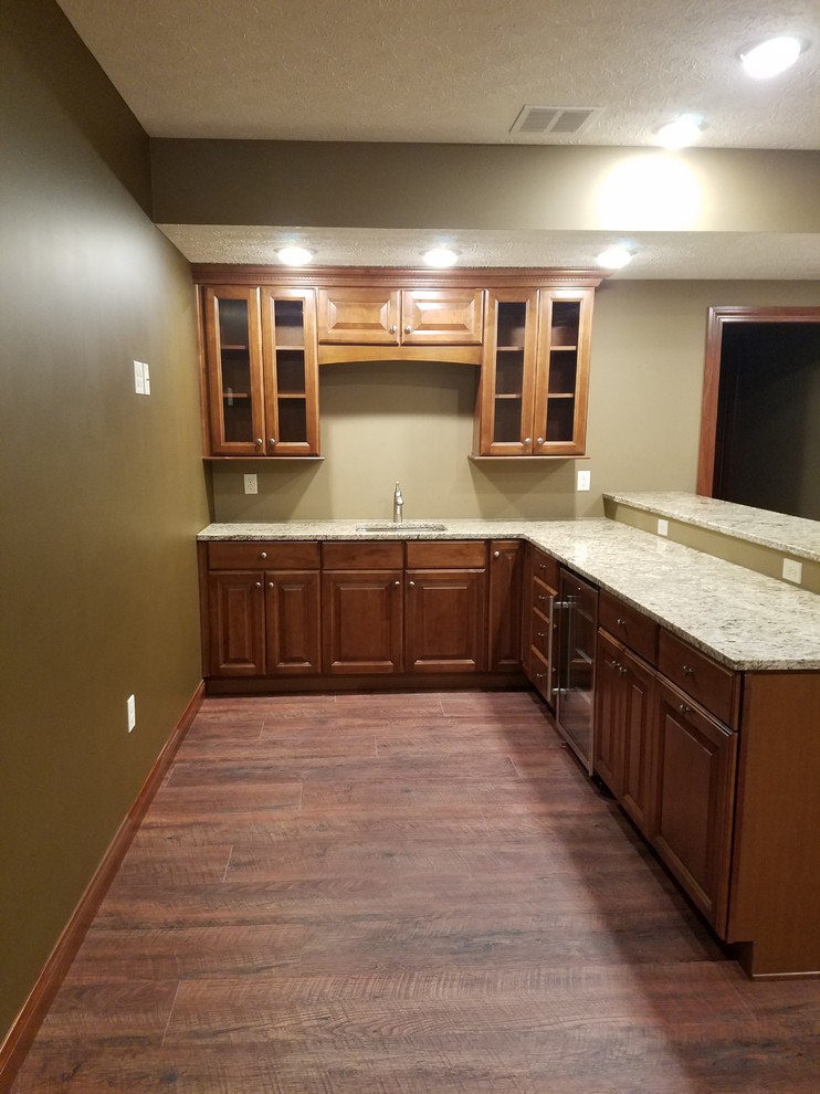 Mid-sized traditional l-shaped wet bar in Other with an undermount sink, raised-panel cabinets, medium wood cabinets, granite benchtops, medium hardwood floors and brown floor.