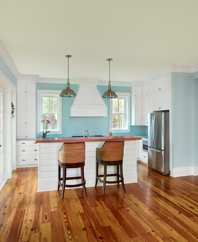 Design ideas for a mid-sized beach style l-shaped eat-in kitchen in Charleston with shaker cabinets, white cabinets, solid surface benchtops, stainless steel appliances, dark hardwood floors, with island, brown floor and blue splashback.