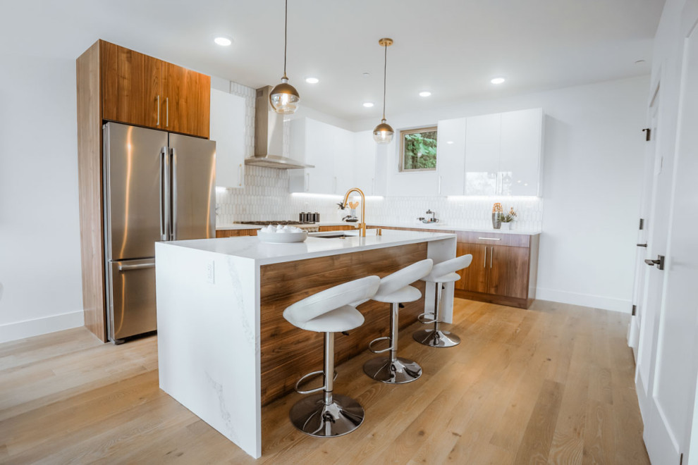 Medium sized contemporary l-shaped kitchen pantry in Seattle with a submerged sink, flat-panel cabinets, medium wood cabinets, marble worktops, metallic splashback, marble splashback, stainless steel appliances, light hardwood flooring, an island, brown floors, white worktops and a coffered ceiling.