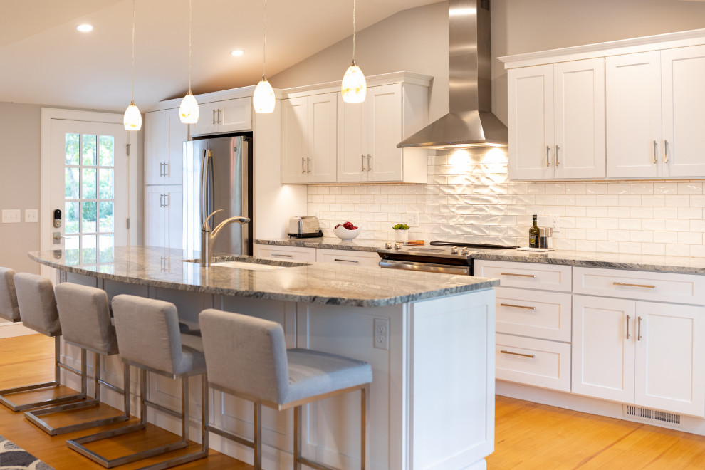 Large transitional single-wall eat-in kitchen in Boston with an undermount sink, shaker cabinets, white cabinets, granite benchtops, white splashback, porcelain splashback, stainless steel appliances, medium hardwood floors, with island, brown floor and multi-coloured benchtop.