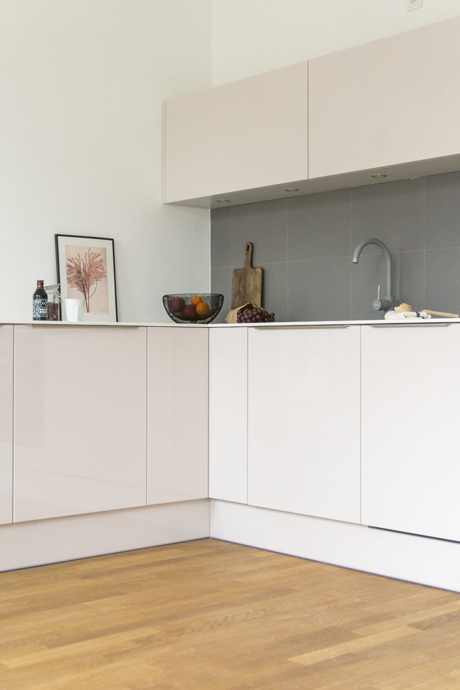 Small modern l-shaped eat-in kitchen in Berlin with a drop-in sink, flat-panel cabinets, purple cabinets, solid surface benchtops, grey splashback, stone tile splashback, panelled appliances, medium hardwood floors, no island, brown floor and white benchtop.