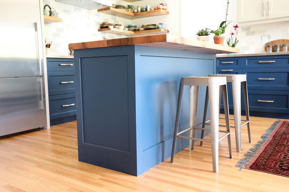 Mid-sized transitional l-shaped light wood floor and beige floor open concept kitchen photo with an integrated sink, shaker cabinets, blue cabinets, stainless steel countertops, ceramic backsplash, stainless steel appliances, an island and gray countertops