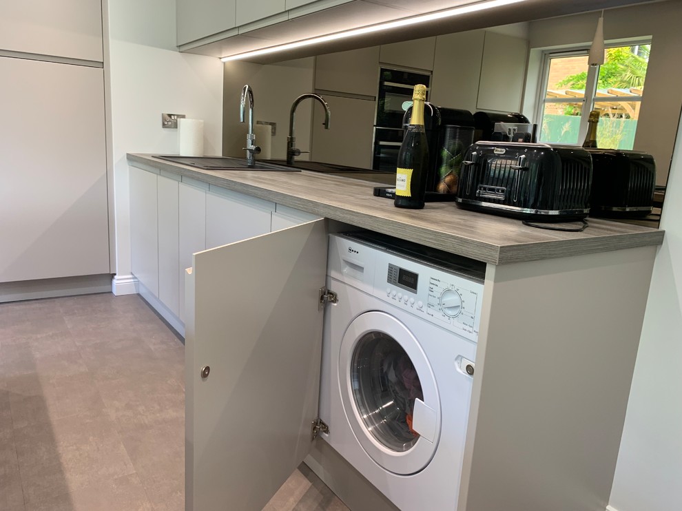 Photo of a mid-sized contemporary l-shaped separate kitchen in Buckinghamshire with a single-bowl sink, flat-panel cabinets, laminate benchtops, glass sheet splashback, panelled appliances, vinyl floors, with island and grey floor.