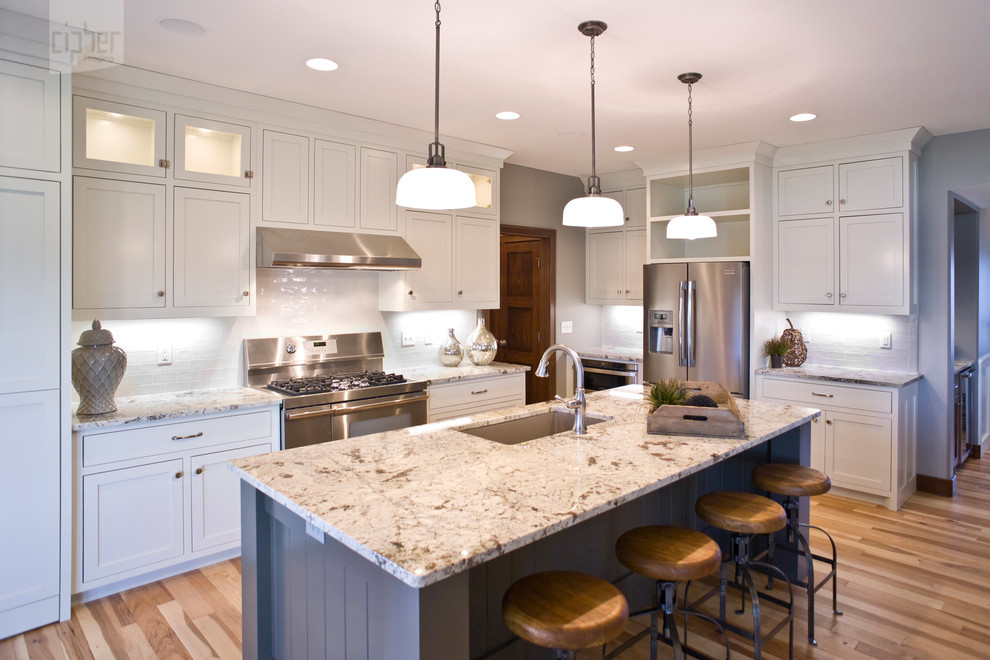 Eat-in kitchen - large transitional l-shaped medium tone wood floor and brown floor eat-in kitchen idea with an undermount sink, recessed-panel cabinets, white cabinets, white backsplash, subway tile backsplash, stainless steel appliances, white walls, an island and granite countertops