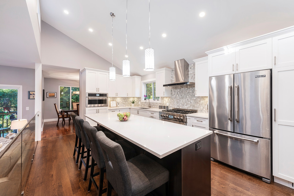 Large transitional l-shaped medium tone wood floor and brown floor eat-in kitchen photo in Vancouver with an undermount sink, shaker cabinets, white cabinets, quartzite countertops, multicolored backsplash, marble backsplash, stainless steel appliances, an island and white countertops