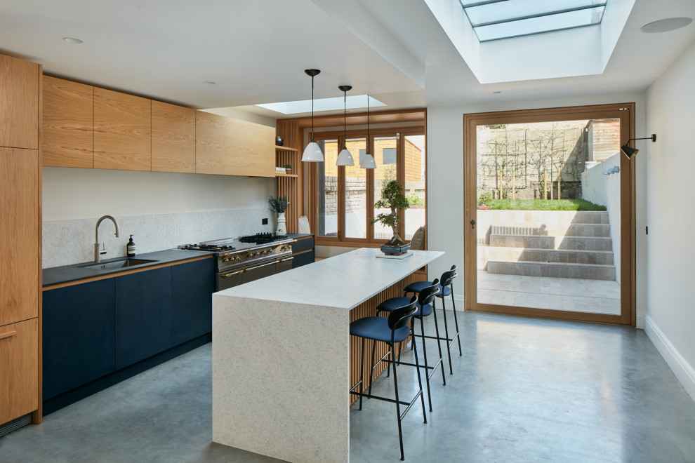 Mid-sized contemporary single-wall eat-in kitchen in London with a drop-in sink, flat-panel cabinets, light wood cabinets, solid surface benchtops, grey splashback, marble splashback, panelled appliances, linoleum floors, with island, grey floor and grey benchtop.