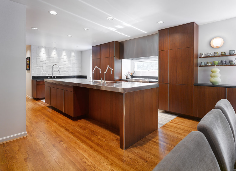 Design ideas for a modern l-shaped eat-in kitchen in Cincinnati with stainless steel benchtops, flat-panel cabinets, dark wood cabinets, stainless steel appliances, an undermount sink, white splashback and ceramic splashback.