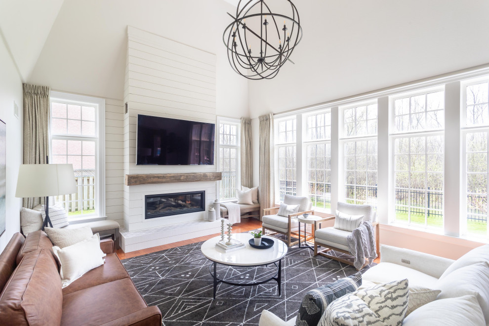 This is an example of a large transitional open concept living room in Toronto with medium hardwood floors, a wood fireplace surround, a wall-mounted tv, white walls, a ribbon fireplace, brown floor, vaulted and planked wall panelling.