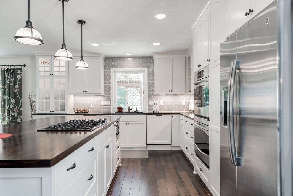 This is an example of a mid-sized country l-shaped eat-in kitchen in Portland with an integrated sink, flat-panel cabinets, white cabinets, wood benchtops, grey splashback, subway tile splashback, stainless steel appliances, dark hardwood floors and with island.