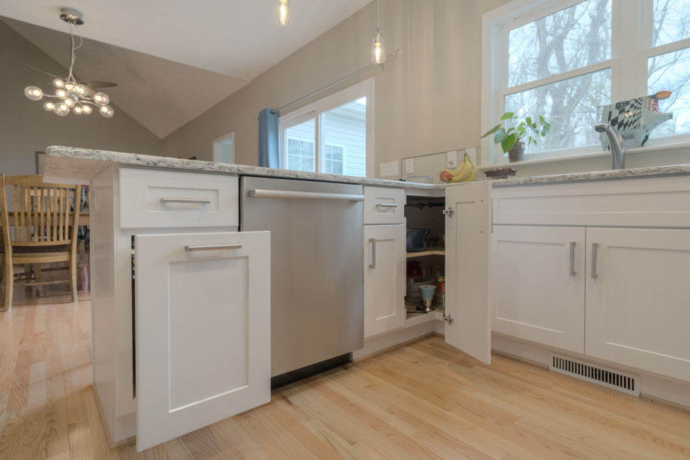 Mid-sized transitional u-shaped light wood floor home design photo with an undermount sink, shaker cabinets, white cabinets, quartz countertops, beige backsplash, glass tile backsplash, stainless steel appliances and a peninsula