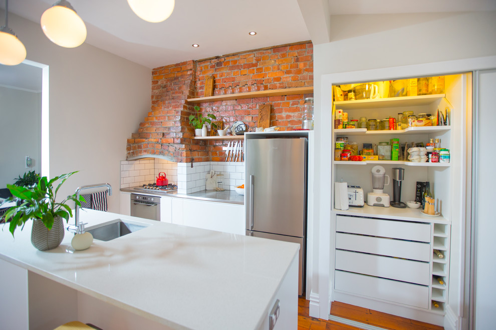 Photo of a mid-sized eclectic galley eat-in kitchen in Wellington with a single-bowl sink, quartz benchtops, white splashback, ceramic splashback, stainless steel appliances, medium hardwood floors and with island.