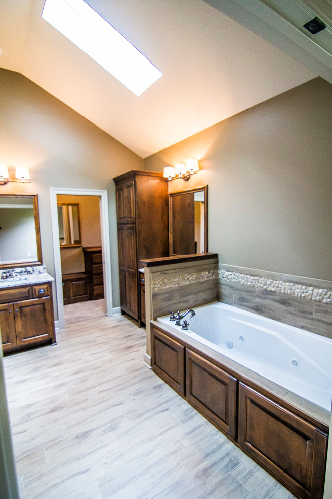 Inspiration for a mid-sized transitional master bathroom in Kansas City with an undermount sink, raised-panel cabinets, medium wood cabinets, granite benchtops, gray tile, porcelain tile, beige walls, ceramic floors and a drop-in tub.