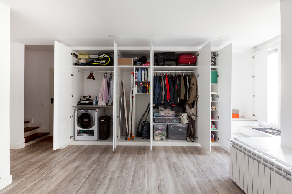 Design ideas for a contemporary laundry room in Madrid with white walls, grey floor and light hardwood floors.