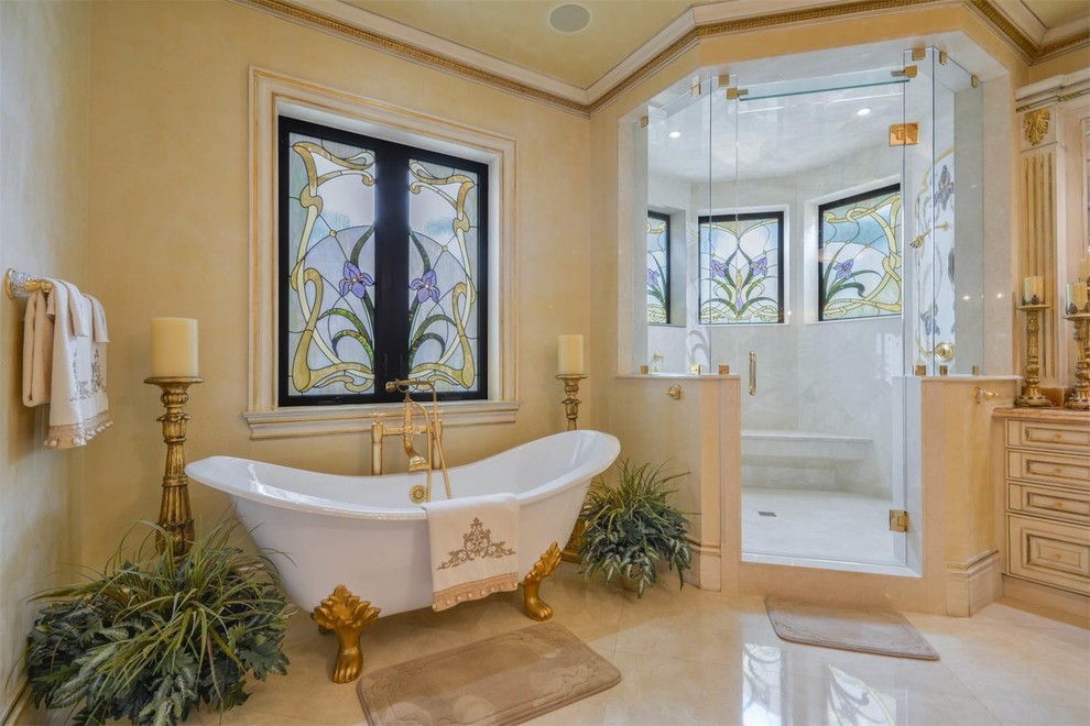 This is an example of an expansive mediterranean master bathroom in Miami with raised-panel cabinets, yellow cabinets, a claw-foot tub, a corner shower, yellow walls, marble floors, a trough sink, granite benchtops and a hinged shower door.