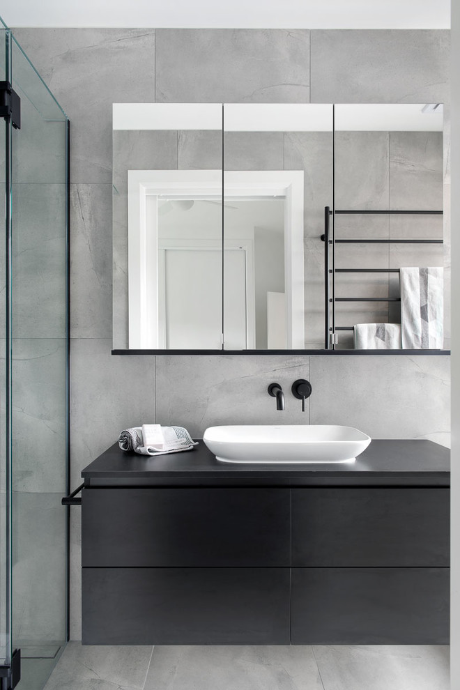 This is an example of a contemporary bathroom in Melbourne with black cabinets, cement tile, grey walls, cement tiles, a vessel sink, laminate benchtops, grey floor, black benchtops, flat-panel cabinets, gray tile and a hinged shower door.