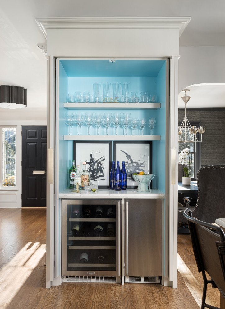Inspiration for a small transitional single-wall seated home bar in New York with a drop-in sink, white cabinets, quartz benchtops, white splashback, marble splashback, medium hardwood floors, brown floor, white benchtop and open cabinets.