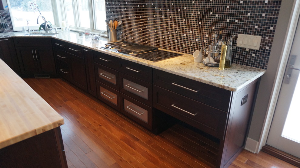 Contemporary l-shaped kitchen in Cleveland with an undermount sink, shaker cabinets, dark wood cabinets, granite benchtops, mosaic tile splashback, stainless steel appliances, medium hardwood floors and with island.