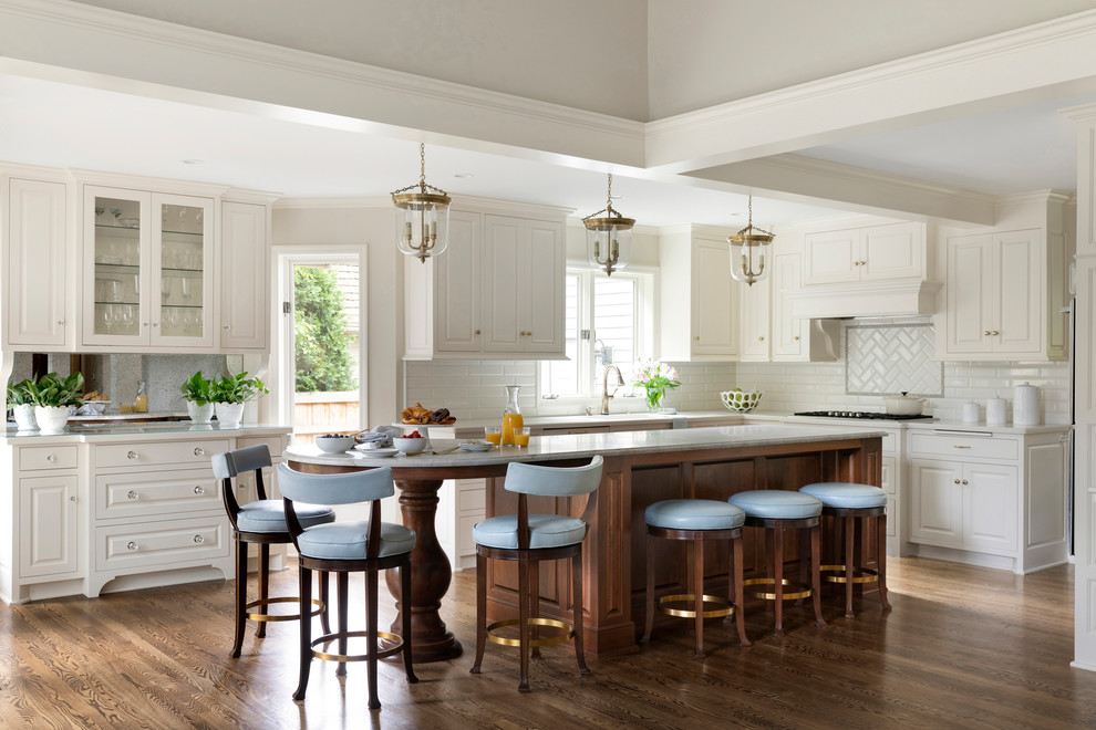 Photo of a traditional l-shaped open plan kitchen in Minneapolis with raised-panel cabinets, white cabinets, white splashback, subway tile splashback, dark hardwood floors, with island, brown floor, white benchtop and coffered.