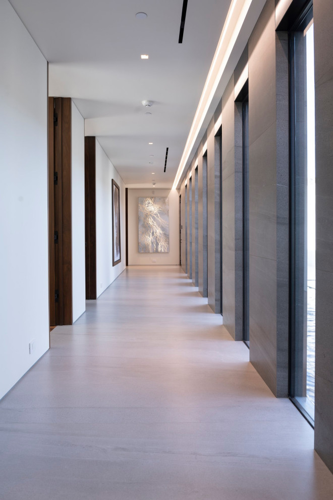 Cette photo montre un grand couloir moderne avec un mur gris, un sol en carrelage de porcelaine, un sol blanc et un plafond décaissé.