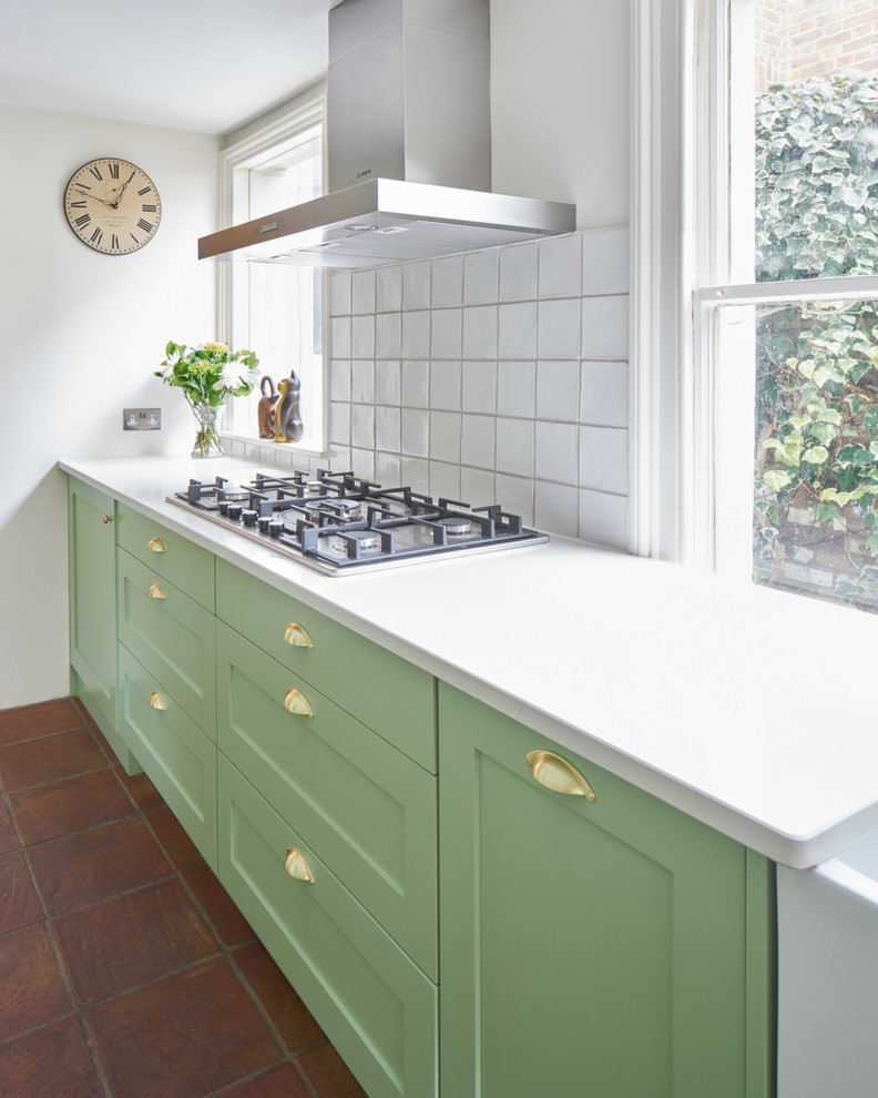 Photo of a small eclectic galley kitchen in London with a farmhouse sink, shaker cabinets, green cabinets, quartzite benchtops, white splashback, ceramic splashback, panelled appliances and terra-cotta floors.